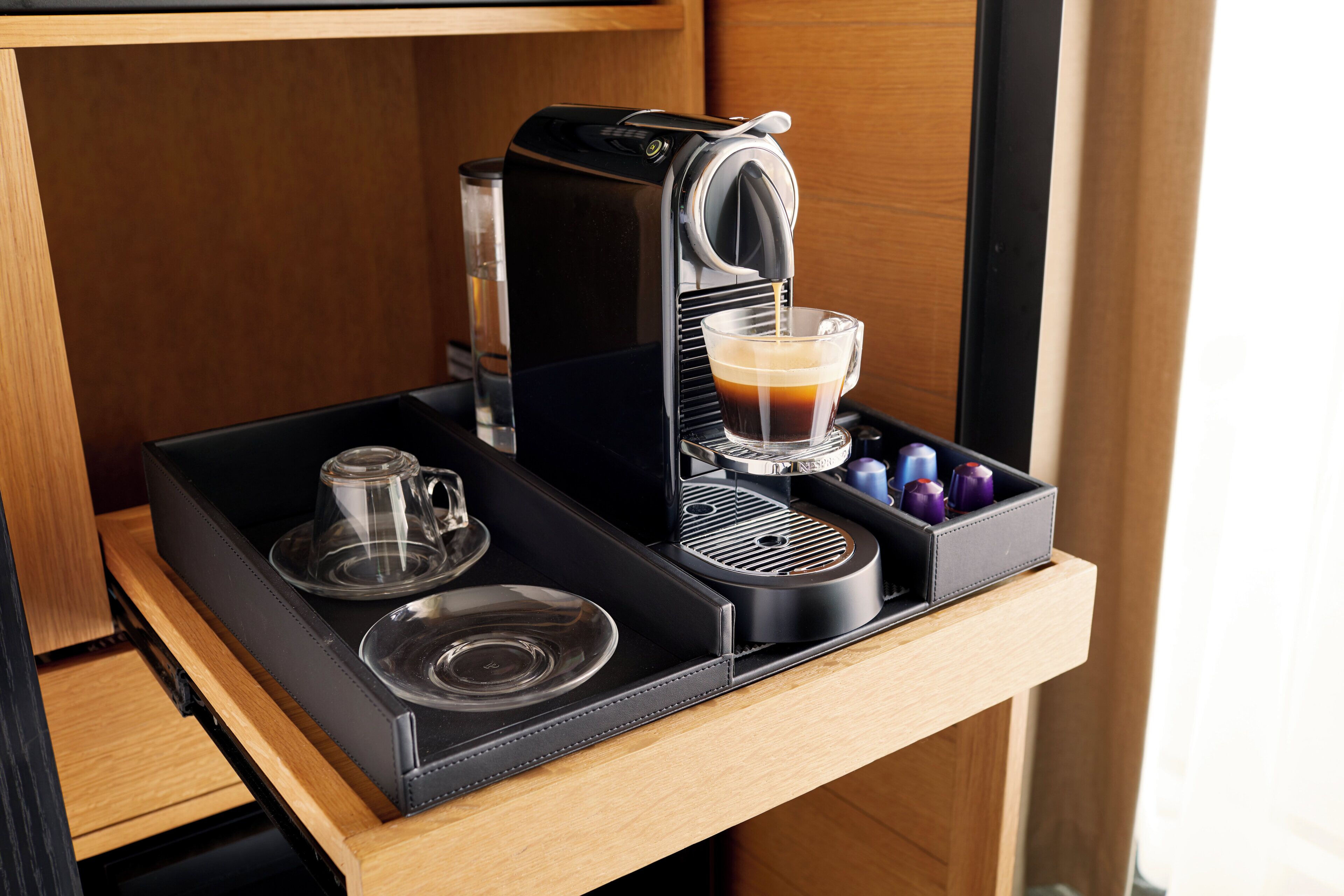 A compact coffee machine with a glass cup and a coffee pot on a wooden countertop.