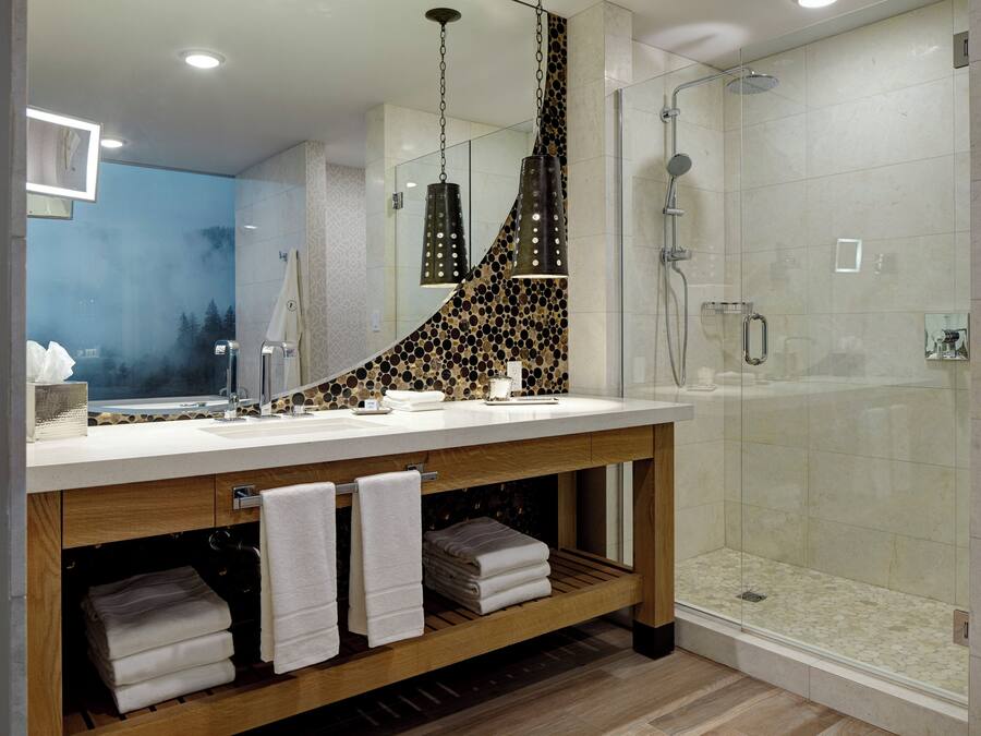 Un bagno moderno con uno specchio grande, un mobile vanità in legno, una doccia con pareti in vetro e uno schienale piastrellato.