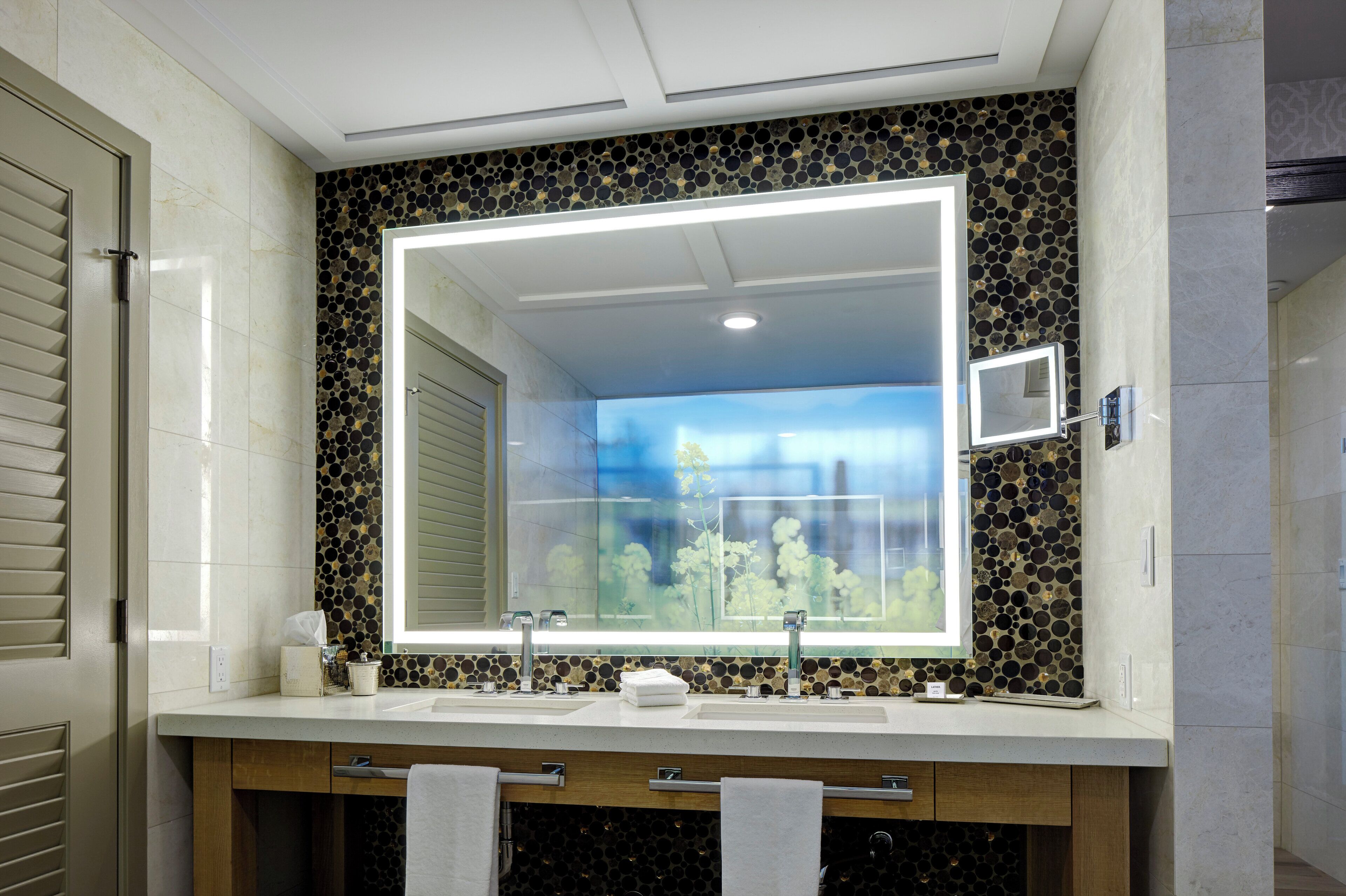 A bathroom with a large mirror, two sinks, and a decorative mosaic wall.