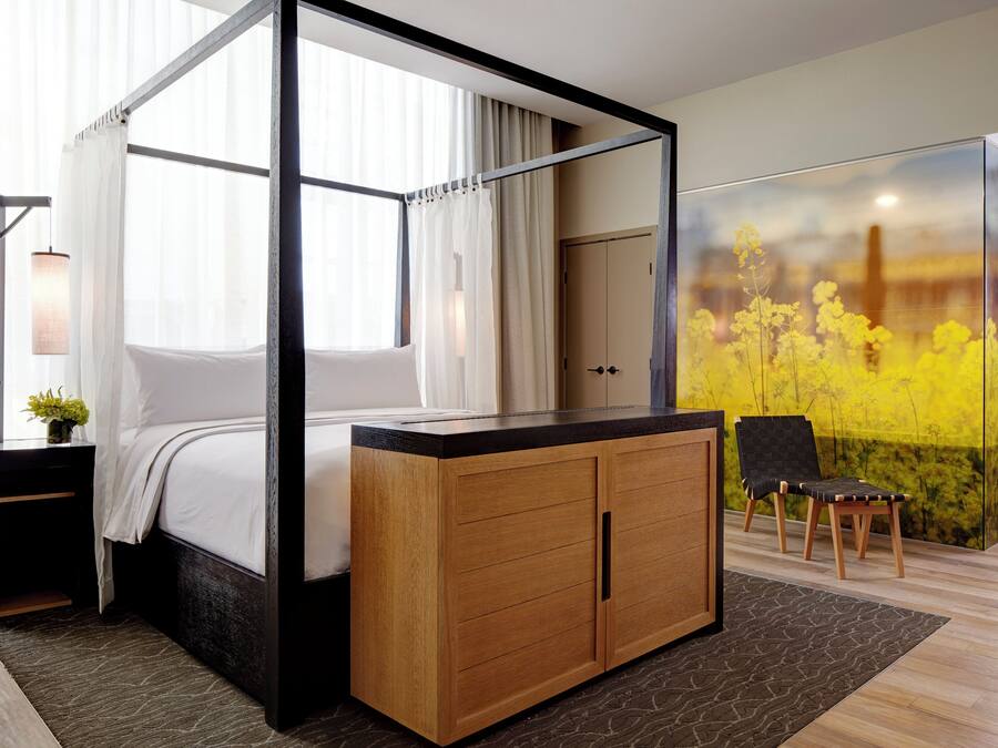 Una cama con dosel de madera, un armario, una silla y un ventanal con cortinas.