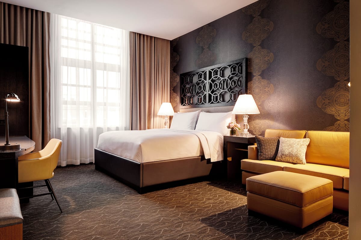 A hotel room with a bed, a sofa, a desk, and a lamp.