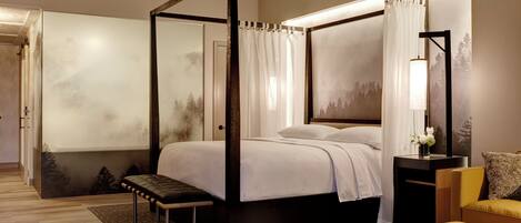 Una cama con dosel y cortinas, un banco, una mesita de noche con lámpara y una silla.