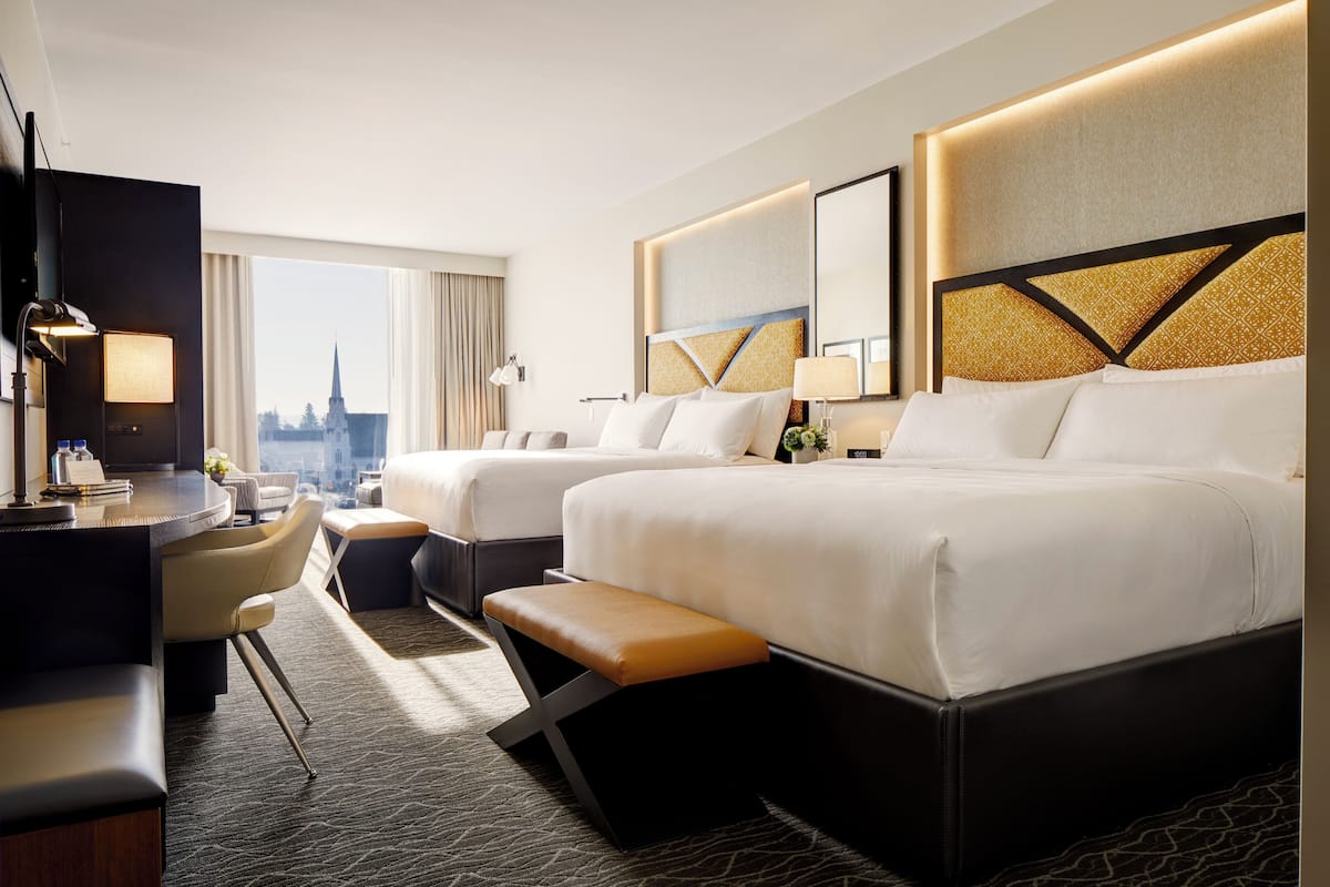 A hotel room with two beds, a desk, and a view of a cityscape.