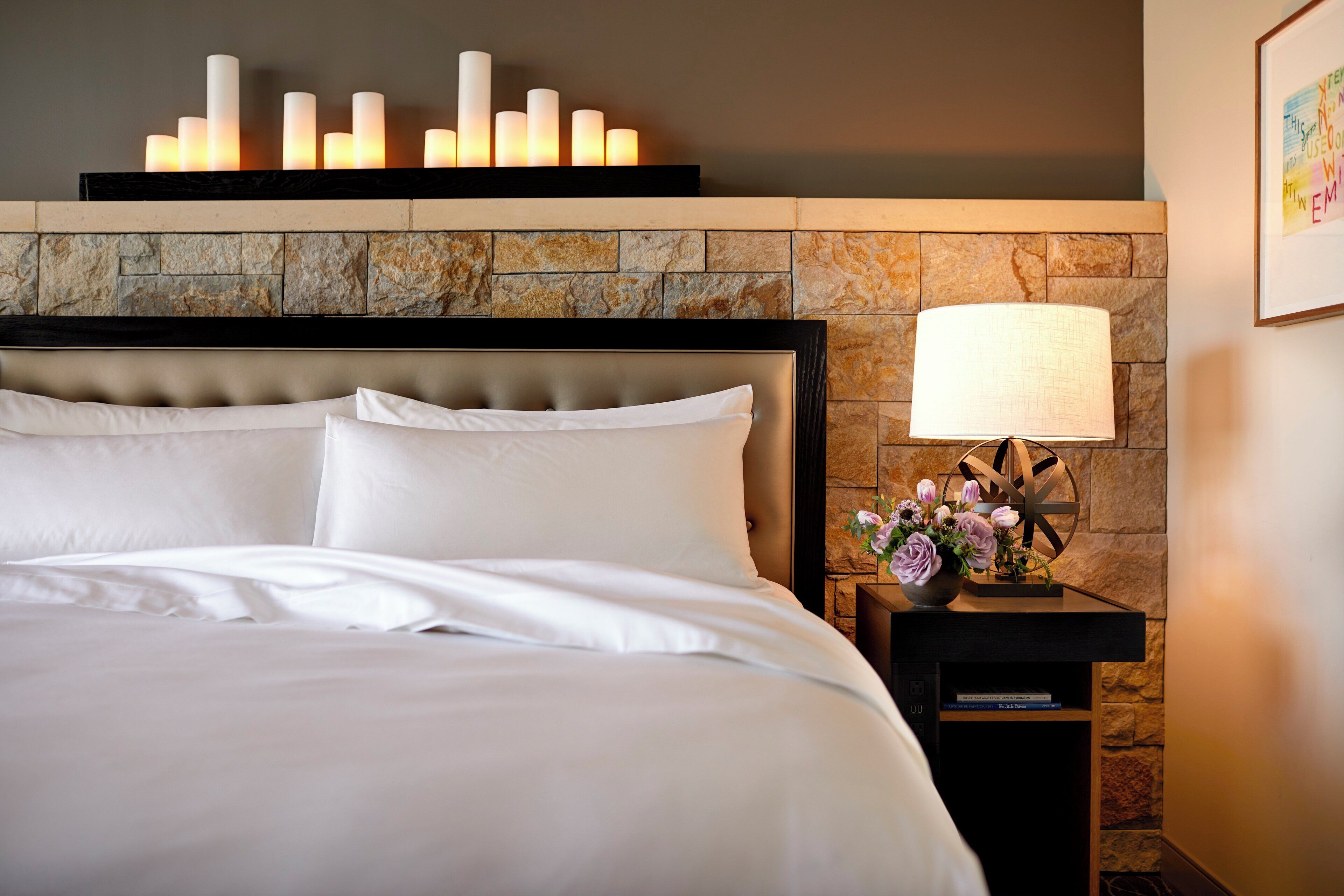 A neatly made bed with white linens, a headboard, and a wall-mounted candle display above it.