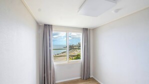 A corner room with a large window, white walls, and wooden flooring. - Kensington Resort Jeju Hanlim (Jeju City)