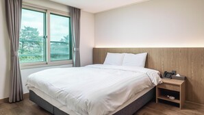 A modern bedroom with a large bed, a nightstand, and a window with curtains. - Kensington Resort Jeju Hanlim (Jeju City)