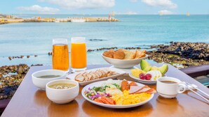 A breakfast table with croissants, fruit, eggs, and coffee, overlooking a coastal view with rocks and a lighthouse. - Kensington Resort Jeju Hanlim (Jeju City)