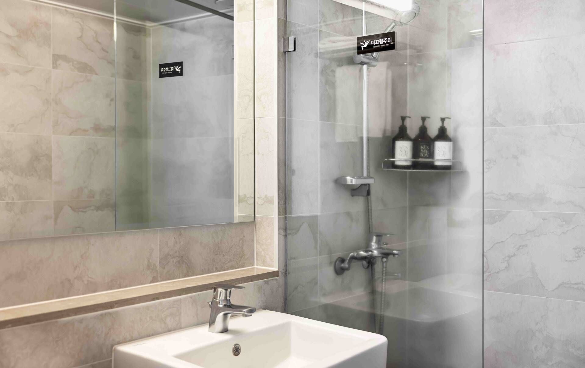 Un baño moderno con ducha de vidrio, lavamanos y estante con artículos de tocador.