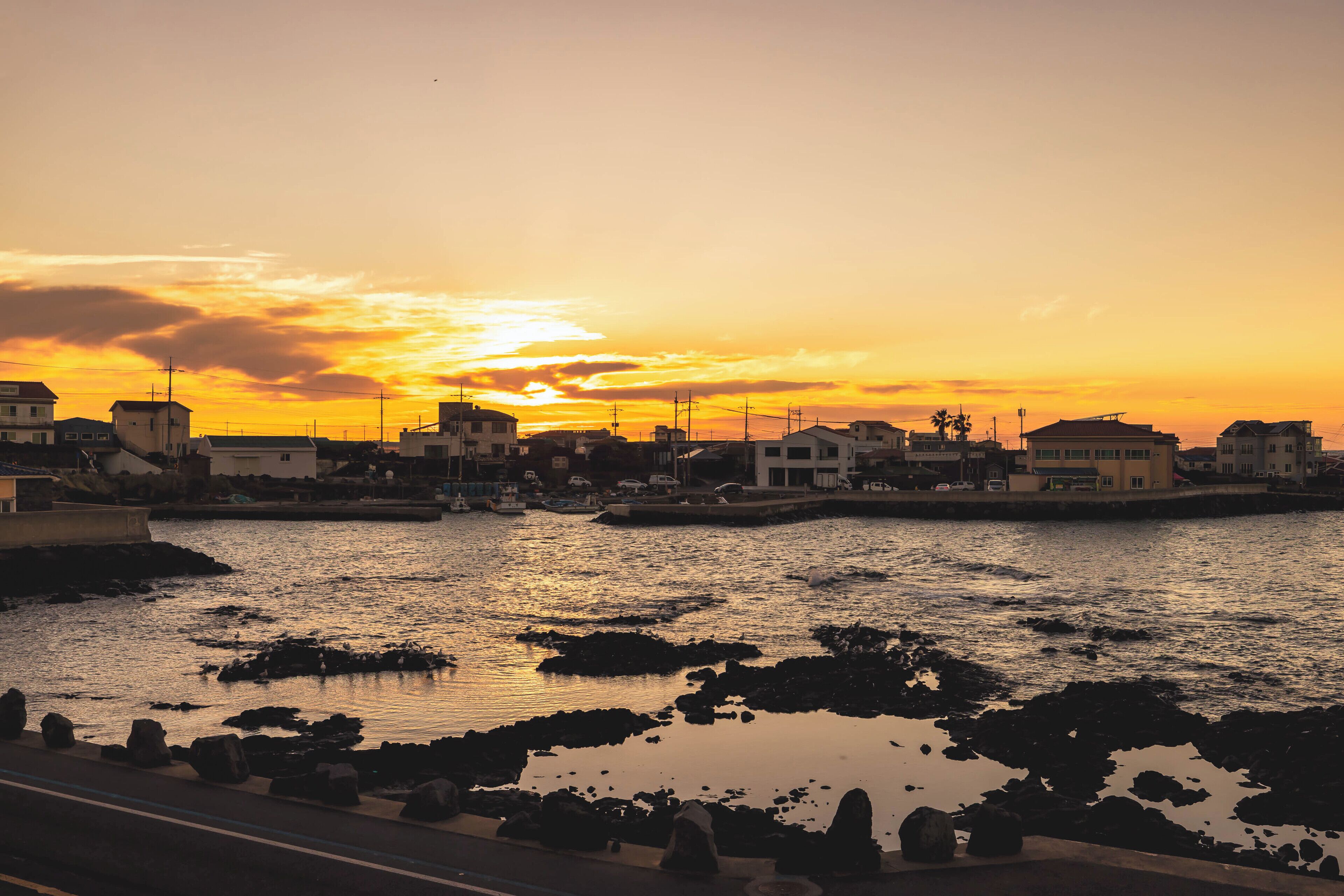 A coastal town at sunset with buildings along the water's edge.
