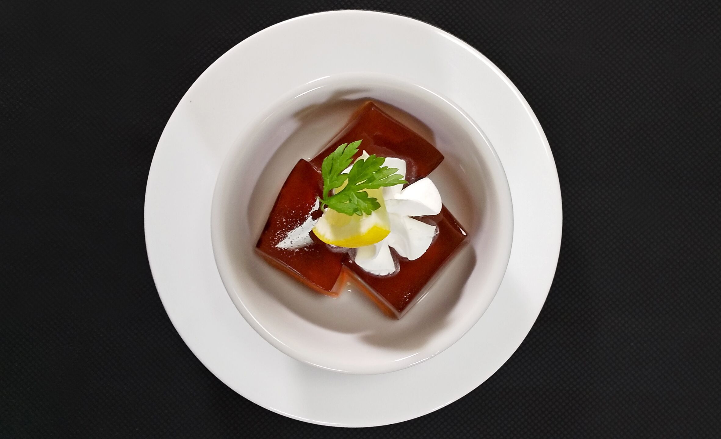 A white plate with a dark-colored dessert, garnished with a leaf and a dollop of cream.