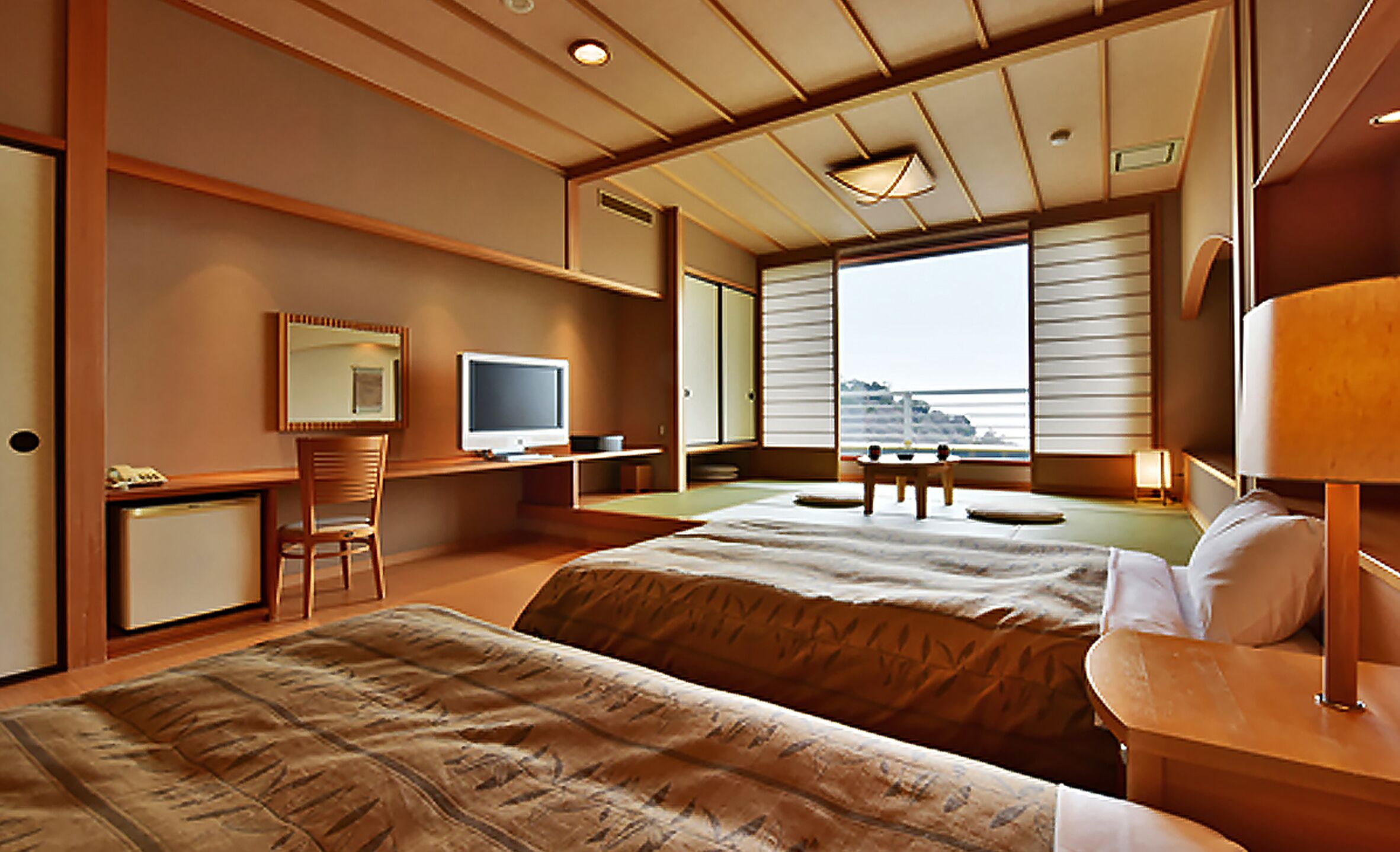 Quarto de hotel com duas camas, uma mesa de trabalho com televisão, uma cadeira e vista para o mar.