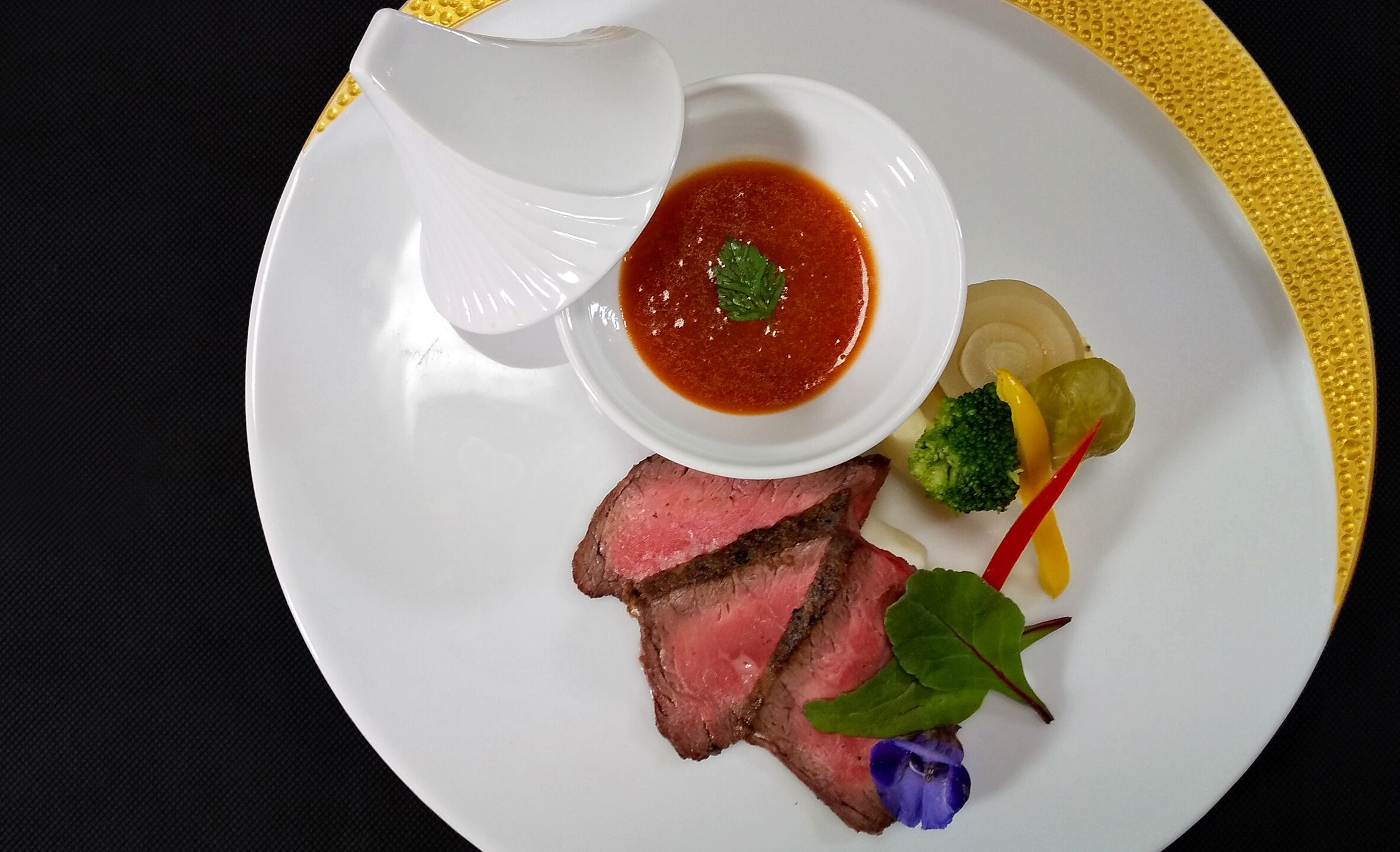 A plate with sliced meat, vegetables, and a small bowl of sauce.