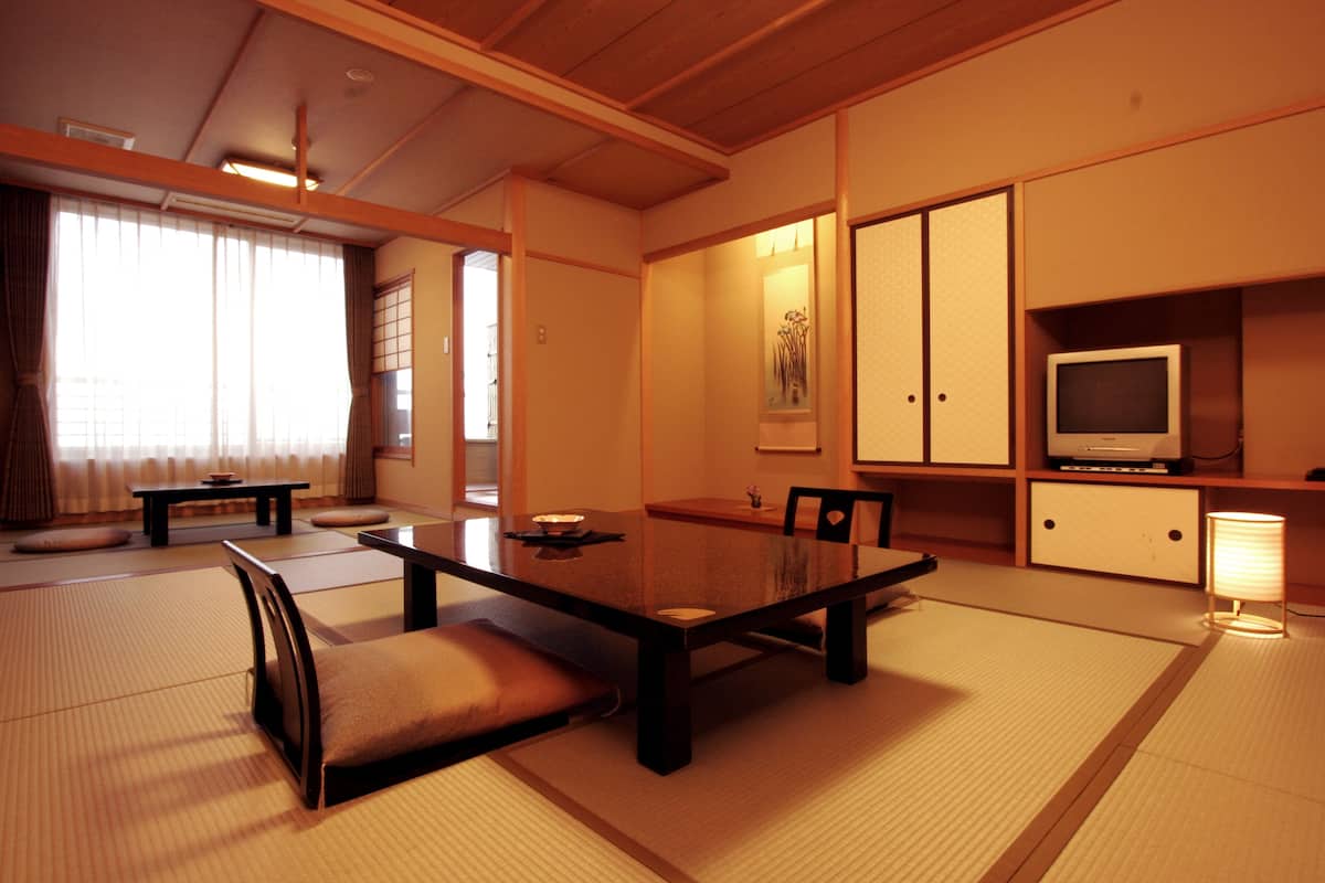 Ett traditionellt japanskt rum med tatamimattor på golvet, ett lågt bord med kuddar, en tv och skjutdörrar.