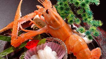 A lobster with a decorative shell and a small bowl of white substance, possibly a sauce, with green foliage in the background.