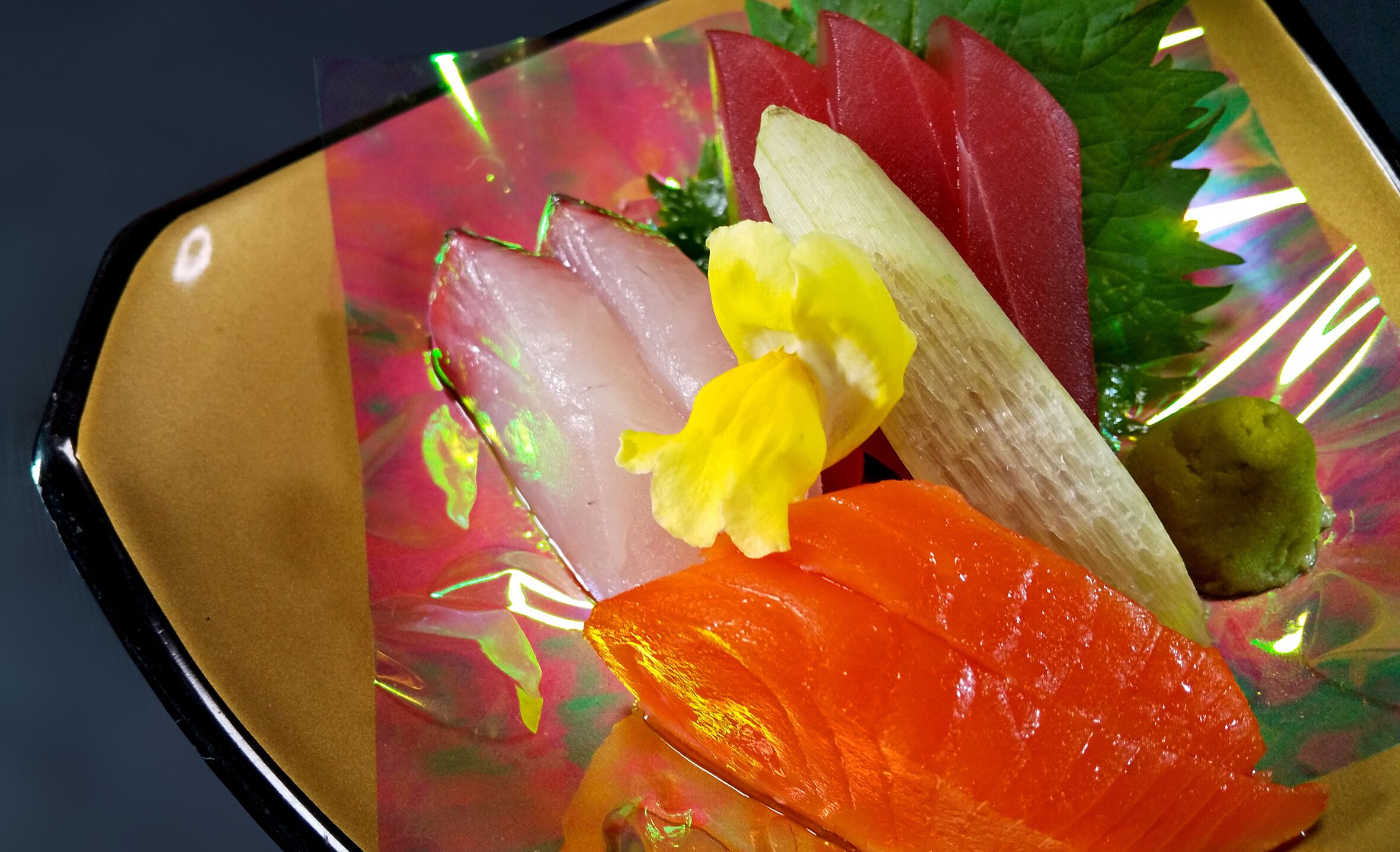 A plate of sashimi with various types of fish and a yellow flower garnish.