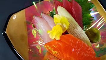 A plate of sashimi with various types of fish and a yellow flower garnish.