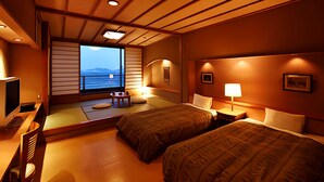Une chambre d’hôtel avec deux lits, une télévision, une fenêtre donnant sur la mer et une petite table avec une lampe.