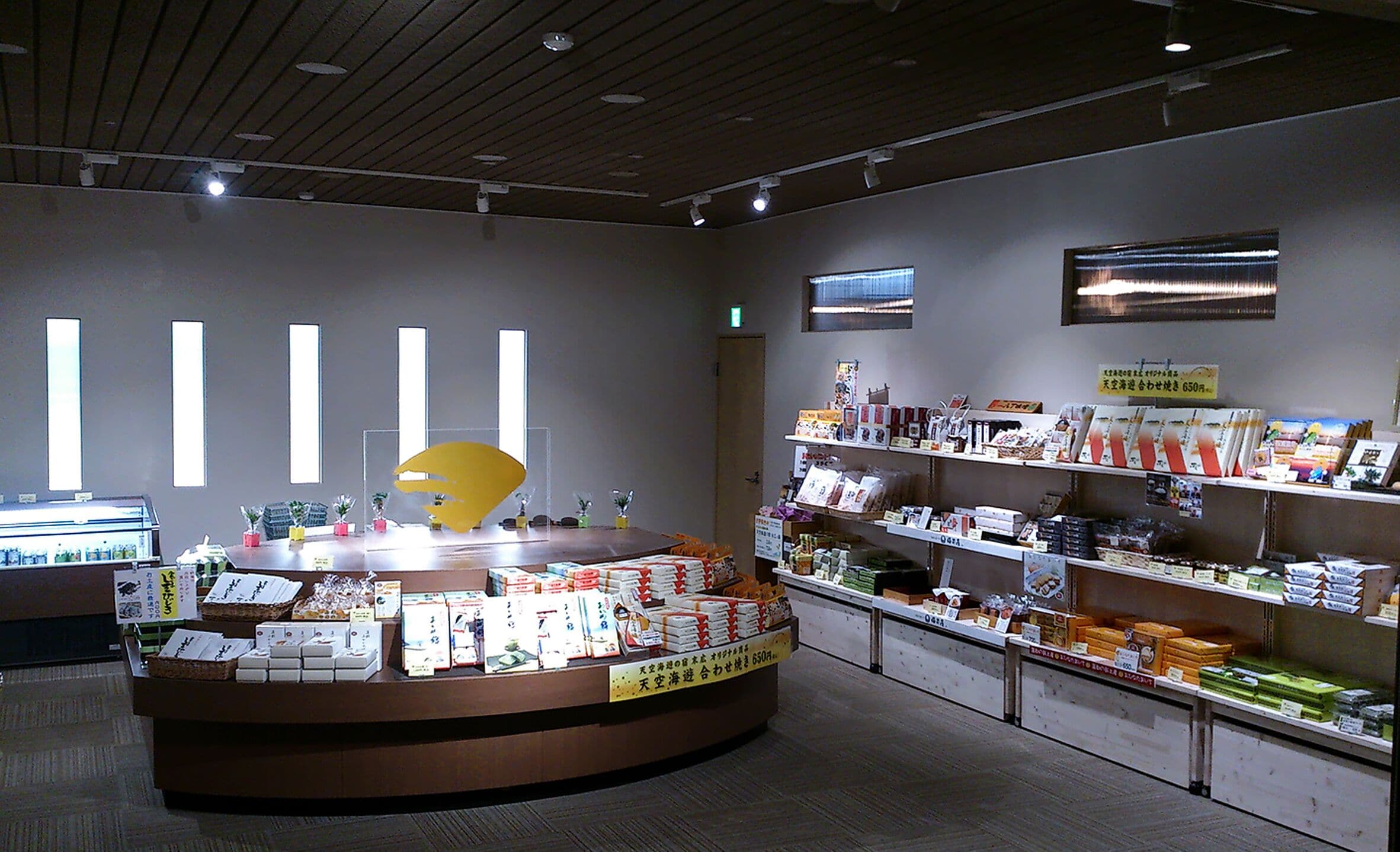 A reception area with a counter displaying various items, a display of books and magazines, and a wall with vertical light fixtures.
