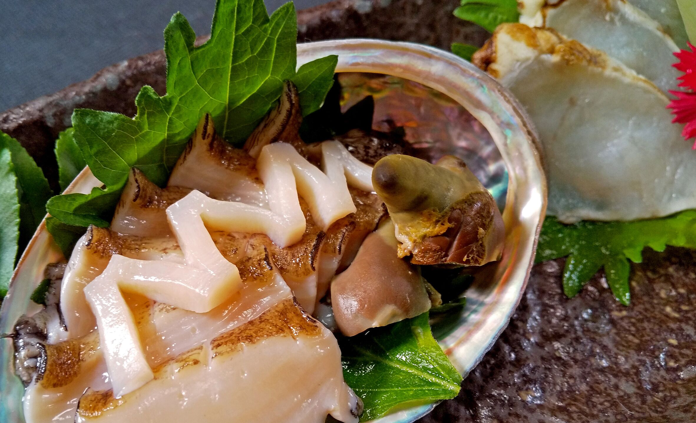 A dish with seafood and greens, possibly a clam or mussel, on a plate with a decorative leaf garnish.