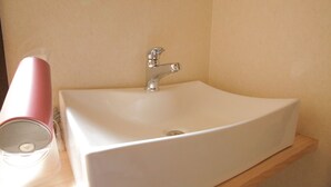 Un baño con un lavabo blanco, un grifo cromado y un secador rosa sobre una estantería de madera.