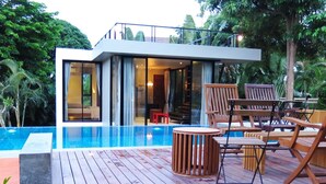 Una casa moderna con piscina, terraza de madera y mobiliario exterior.