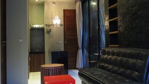 Una sala de estar moderna con un sofá de cuero negro, un reposapiés rojo y una araña.