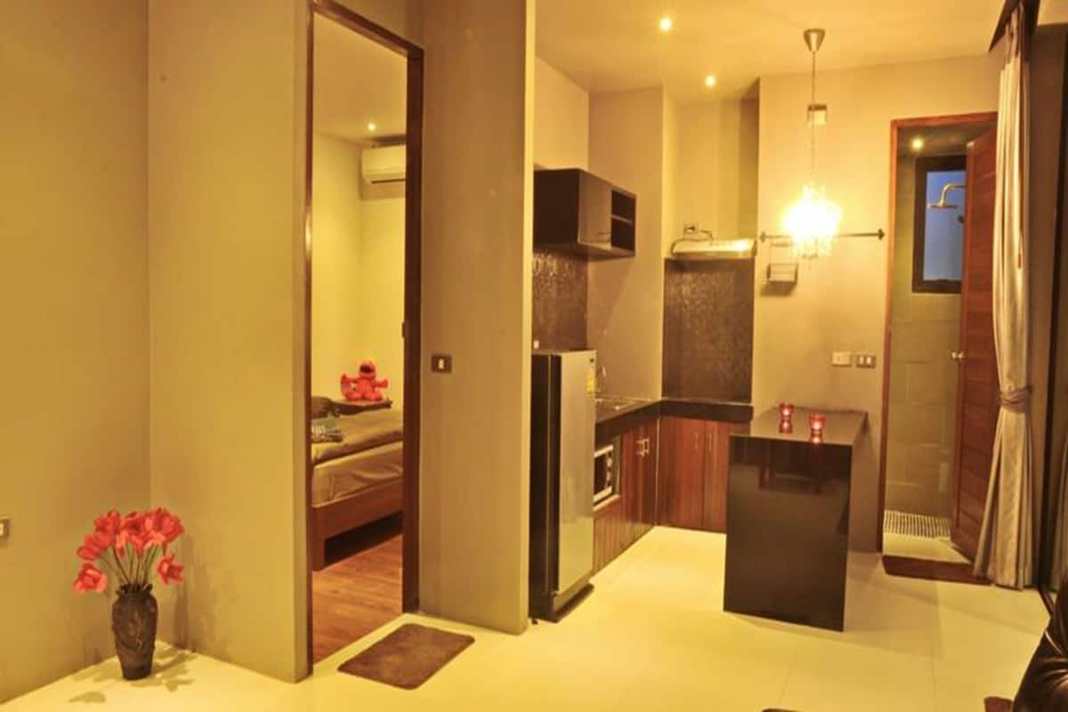 A modern kitchen with a central island, a dining area with a sofa, and a visible bathroom with a shower.