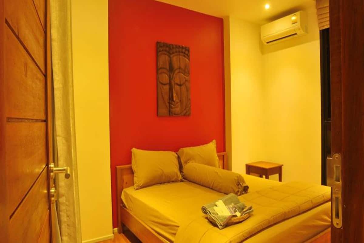 A bedroom with a bed, pillows, a small bedside table, and a wall-mounted air conditioner.