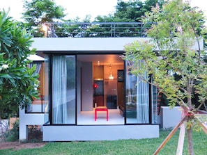 Una casa moderna de dos pisos con fachada de vidrio, un banco rojo y un área de comedor visible a través del vidrio.