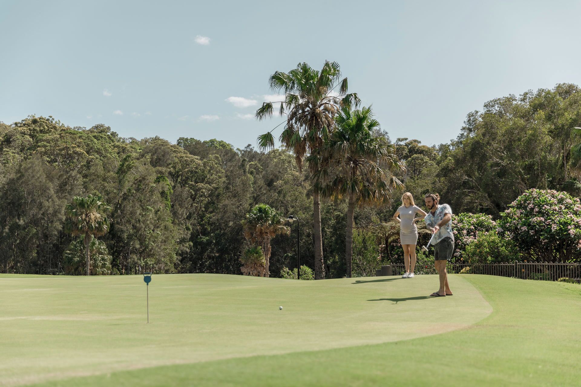 Un campo de golf con cielo despejado, exuberante vegetación y un mástil con la bandera en el green.