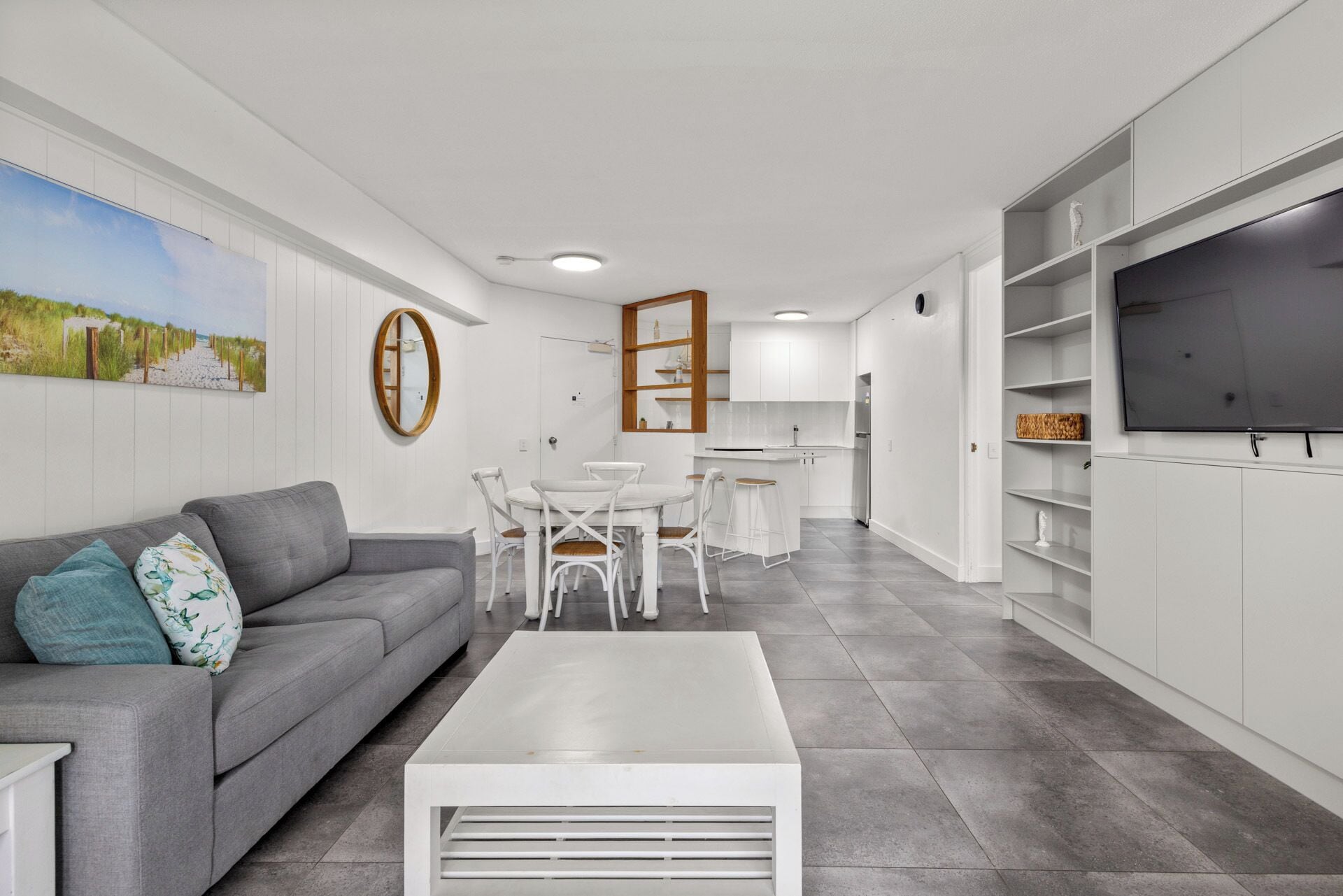 A modern living room with a grey sofa, white coffee table, and a dining area with white chairs.