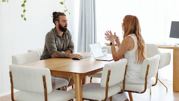 A modern meeting room with a wooden table, white chairs, and a laptop on the table.