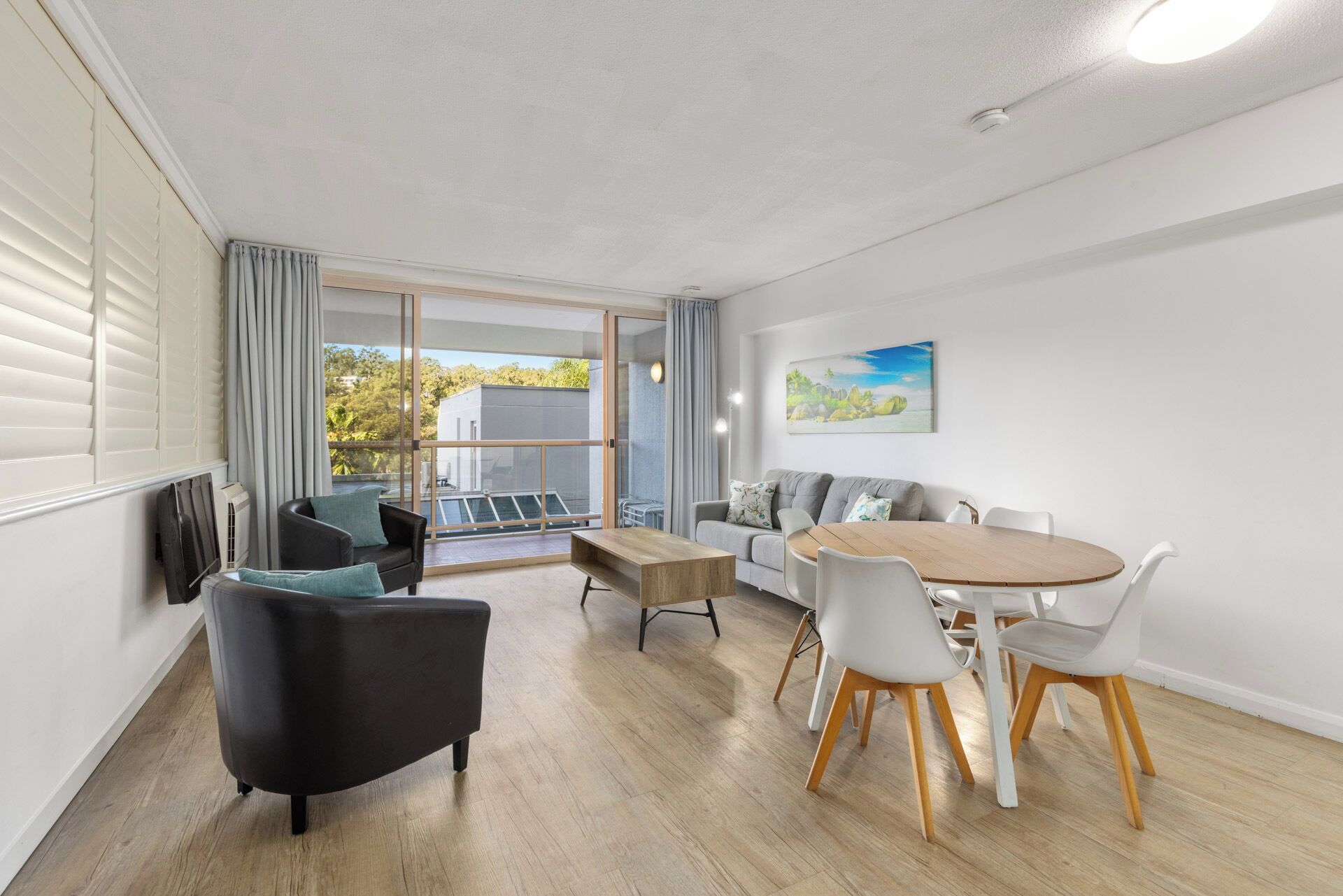 Una sala de estar moderna con un sofá, una mesa de comedor y sillas. Hay un ventanal corredero que da a un balcón.