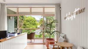 A modern hotel room with a balcony, a desk with a computer, a seating area with a sofa and chairs, and a large potted plant. - Charlesworth Bay Beach Resort (Coffs Harbour)