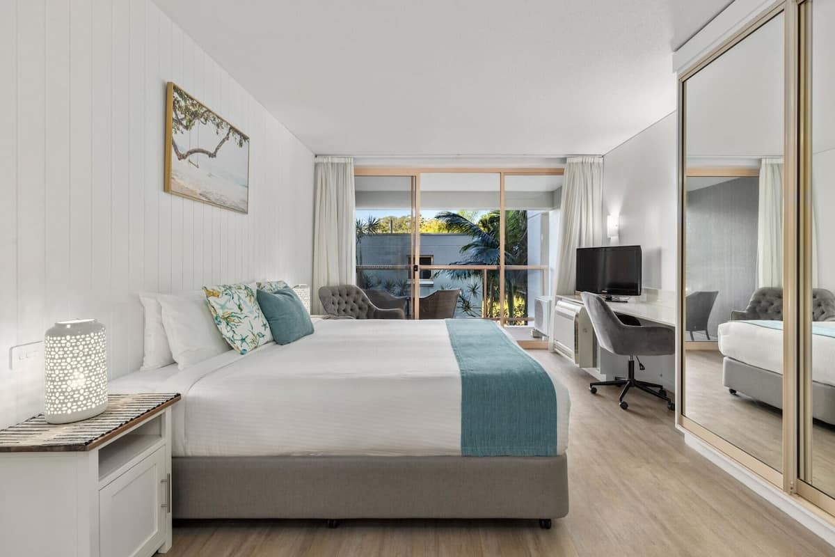 Une chambre d’hôtel moderne dotée d’un grand lit, d’un bureau avec un ordinateur et d’un coin salon avec des fauteuils.