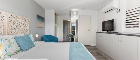 A modern hotel room with a bed, a desk, a TV, and an air conditioning unit.