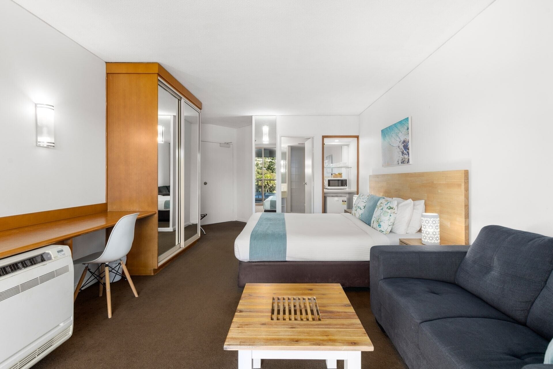 A hotel room with a bed, a sofa, a desk, and a kitchenette.