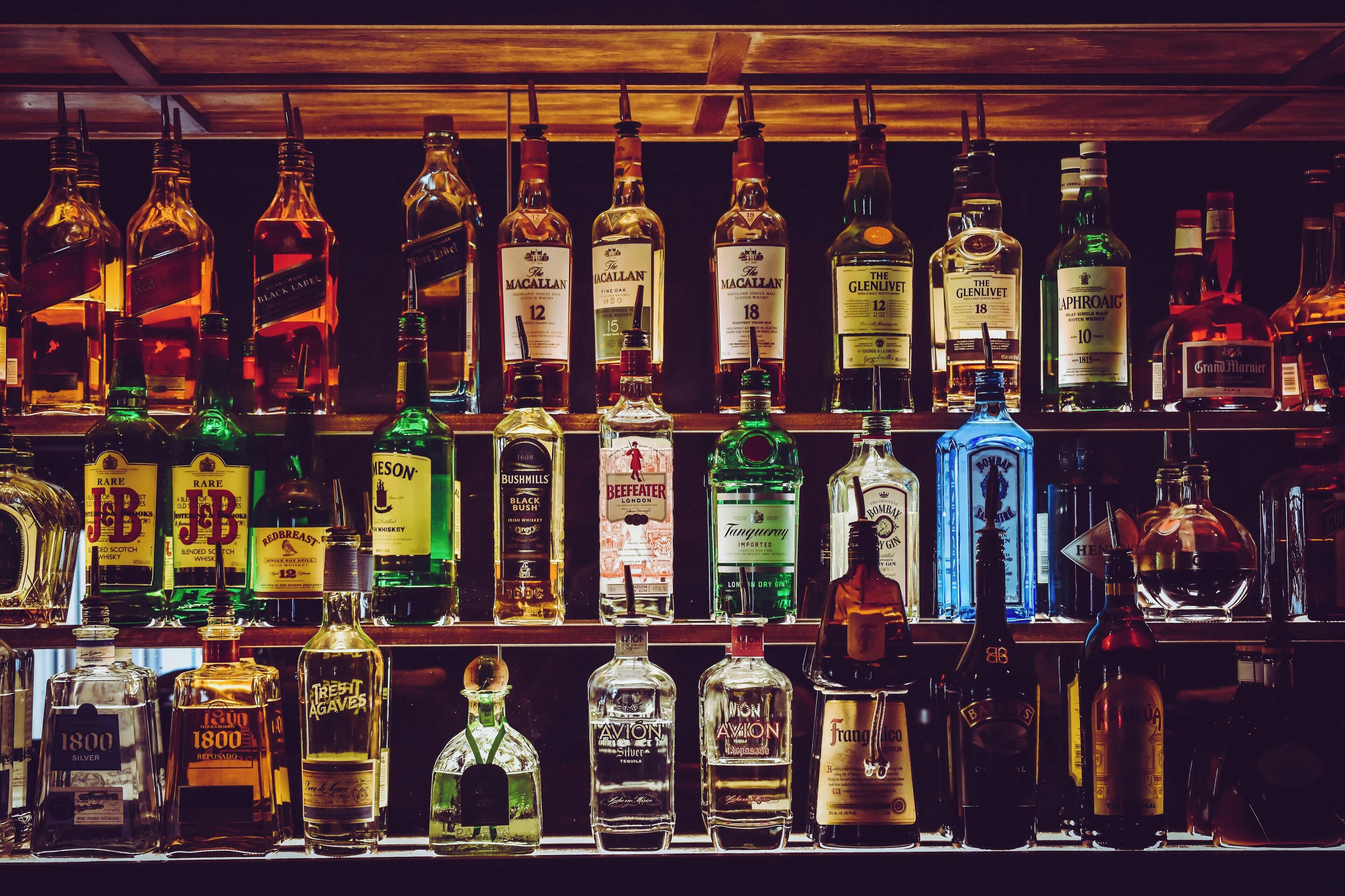 A variety of liquor bottles on shelves in a bar setting.