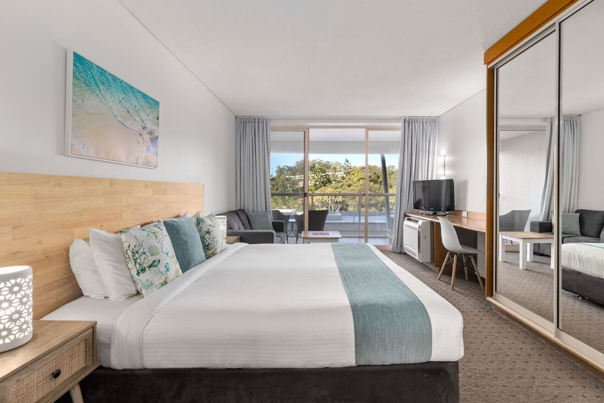 Une chambre d’hôtel avec un grand lit, un bureau avec une chaise, une télévision et un balcon avec vue.