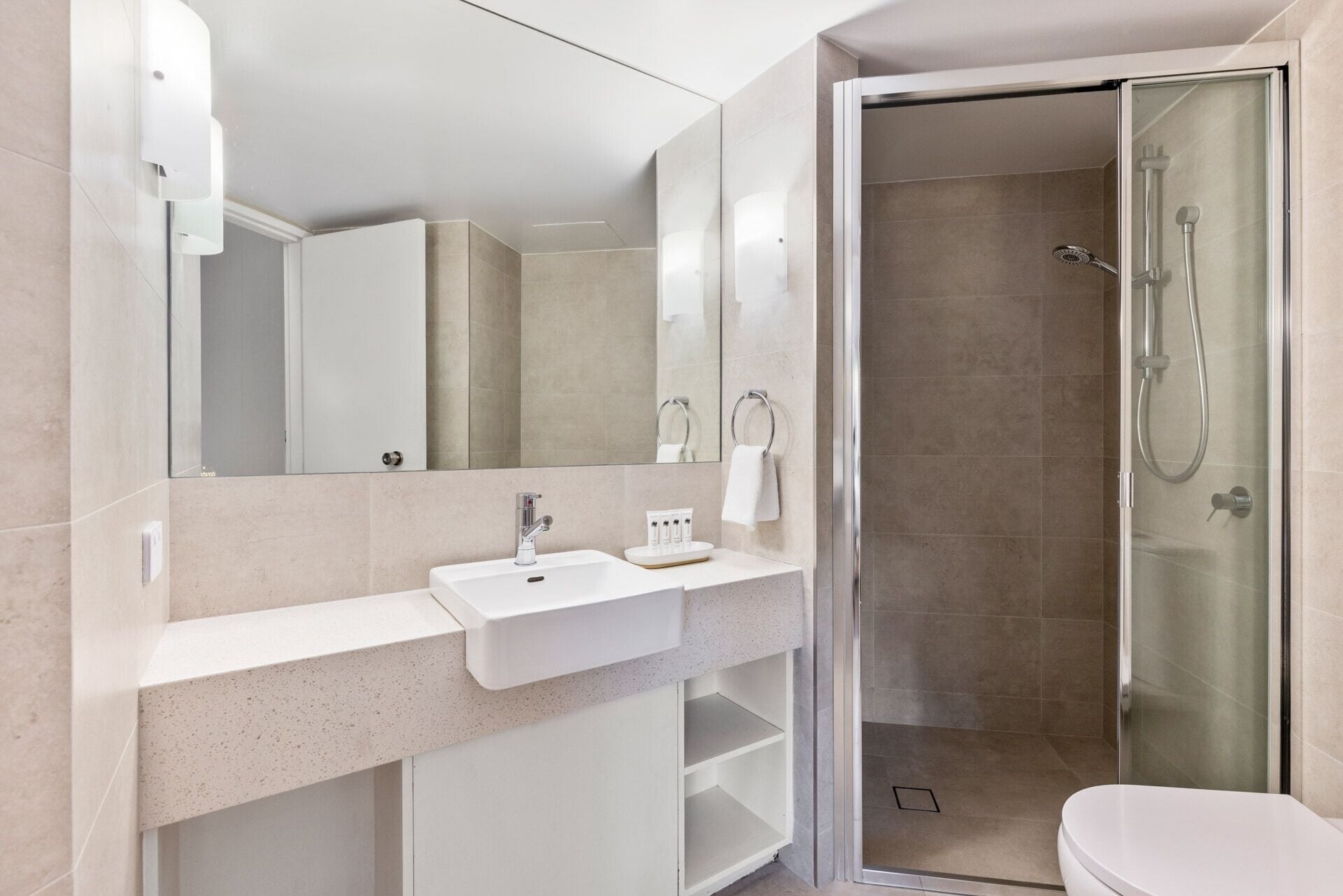 Un baño moderno con lavamanos blanco, un espejo grande y ducha con mampara de vidrio.