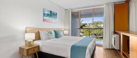 Una habitación de hotel con cama, mesita de noche, lámpara y vistas al exterior.