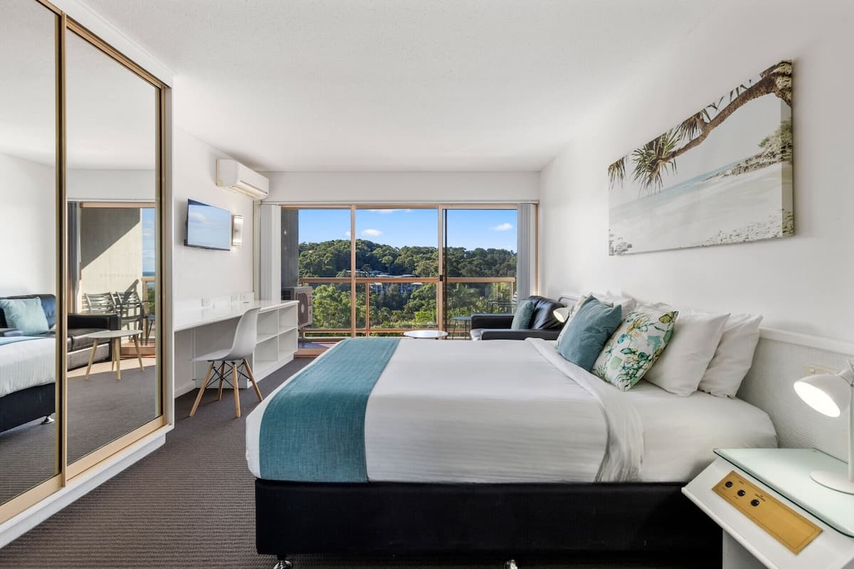 Une chambre d’hôtel moderne dotée d’un grand lit, d’un bureau et d’un balcon offrant une vue panoramique.
