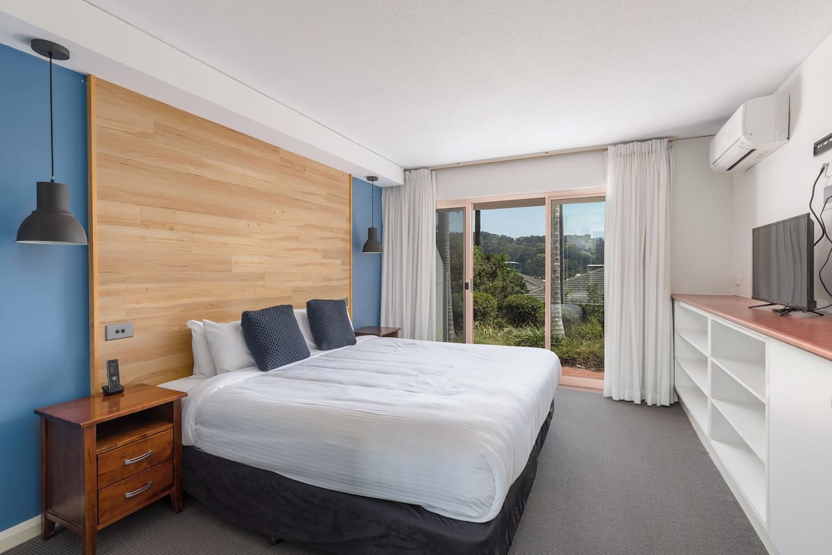 Une chambre d’hôtel moderne, dot ée d’un grand lit, d’un bureau et offrant une vue sur la verdure par la fenêtre.