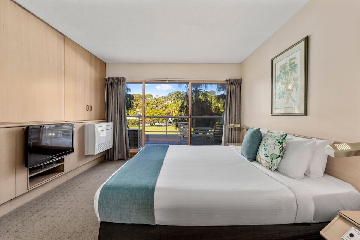 Une chambre d’hôtel avec un lit, une télévision, un bureau et un balcon donnant sur la verdure.
