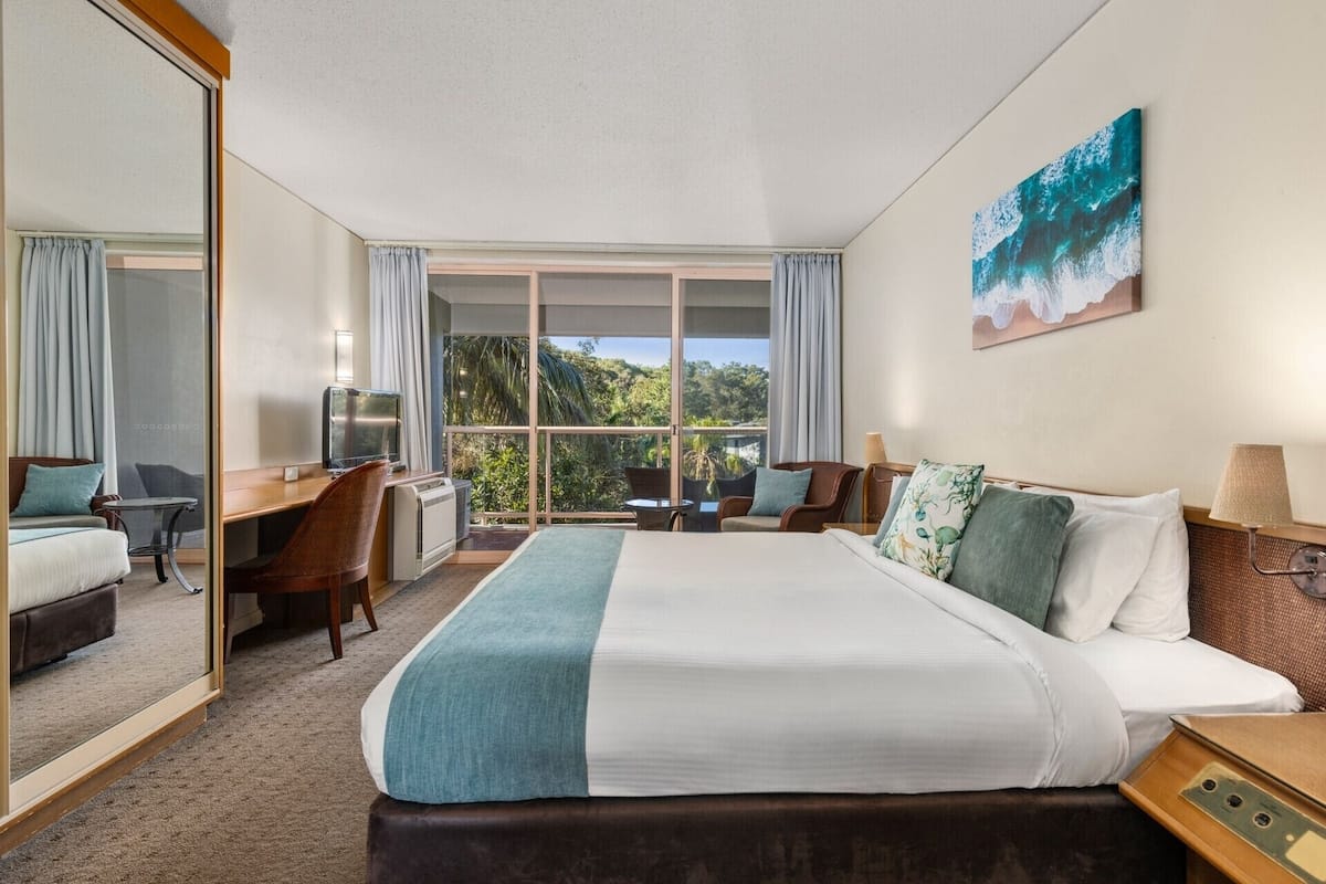 Une chambre d’hôtel avec un grand lit, un bureau, une chaise et une vue sur l’extérieur.