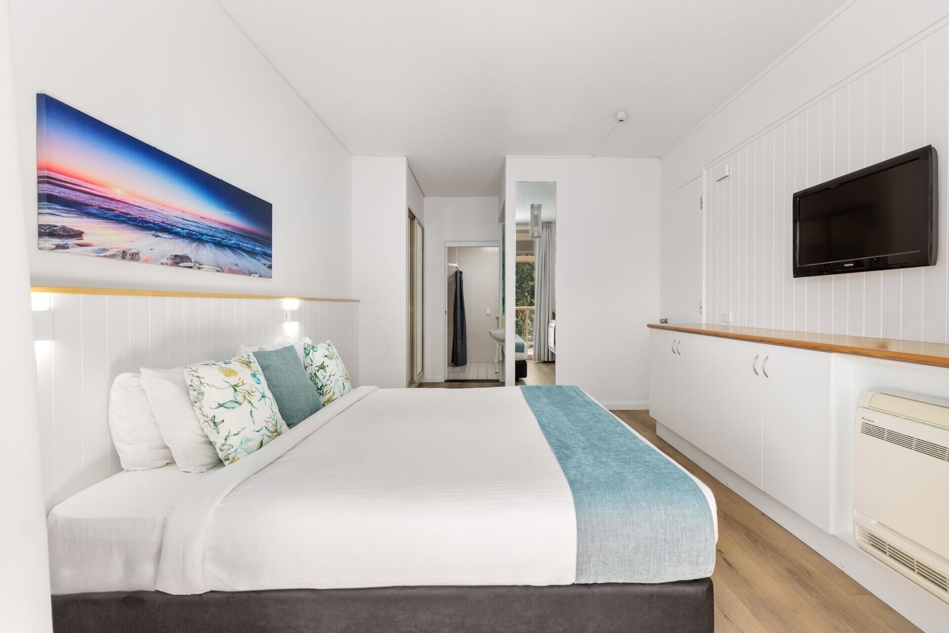 A modern hotel room with a large bed, a TV, and a view of the sea through a window.