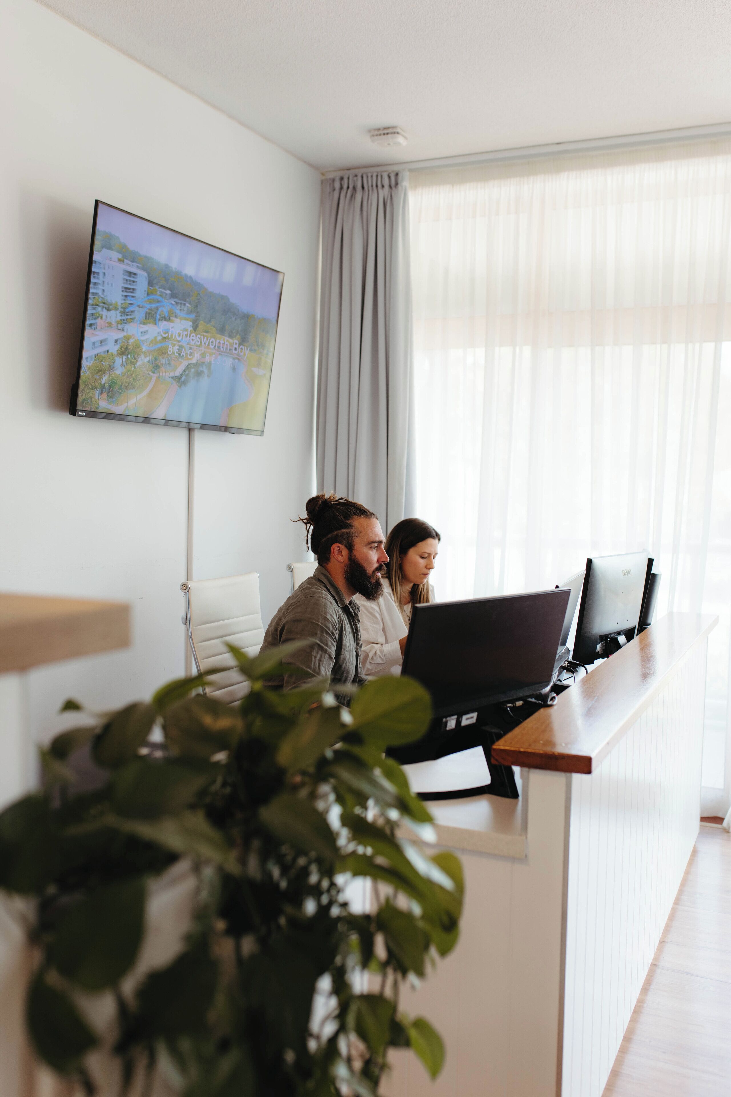Una reception con due persone che lavorano ai laptop, un televisore a schermo piatto sulla parete e un'ampia finestra con tende.