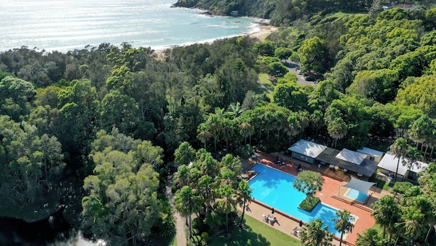 An aerial view of a resort with a swimming pool surrounded by lush greenery and a beach in the background. - Charlesworth Bay Beach Resort (Coffs Harbour)