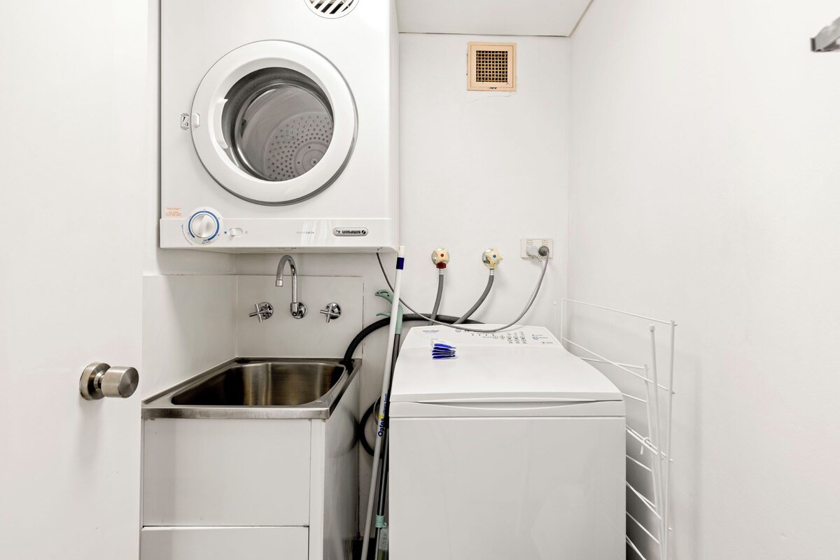 A compact laundry room with a washing machine, a dryer, and a sink with multiple faucets.