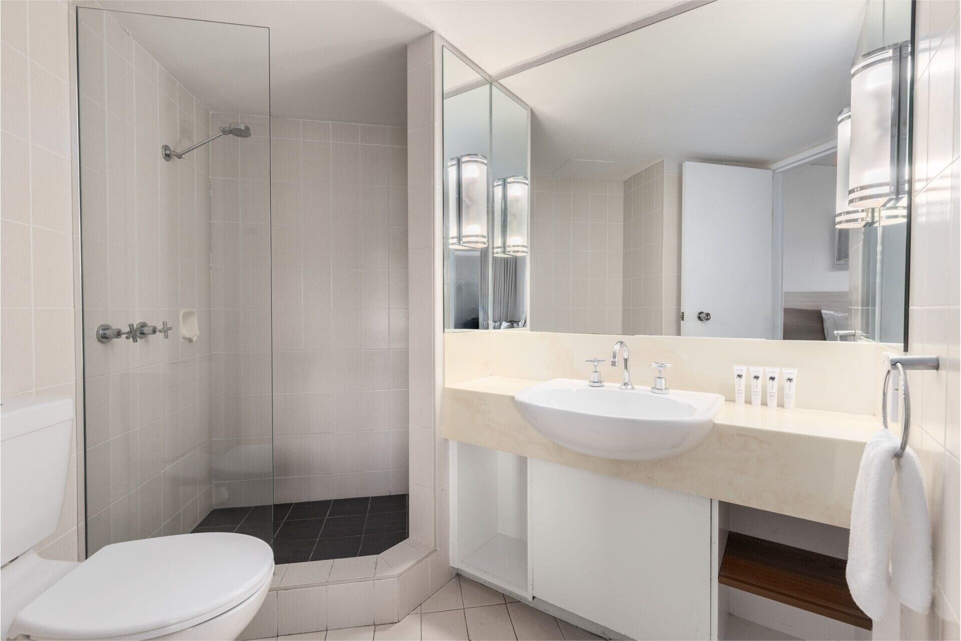 Un baño moderno con cabina de ducha, inodoro y lavabo con un espejo grande.